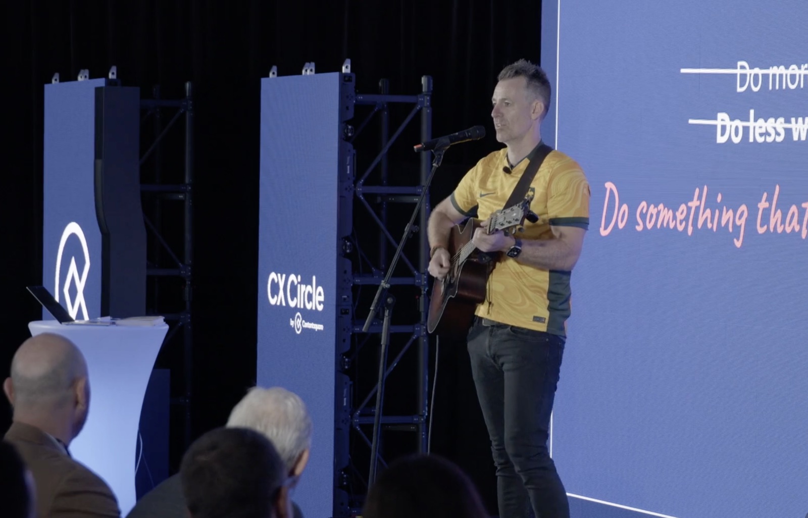 Dave Anderson closing a CX Circle keynote with a guitar, in a Socceroos jersey